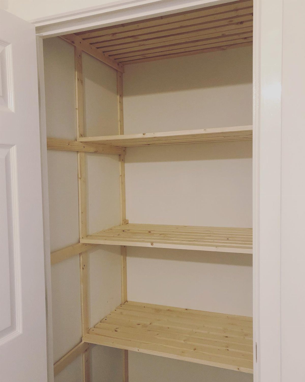 Light wooden slatted shelves installed inside a white closet with a matching slatted ceiling.