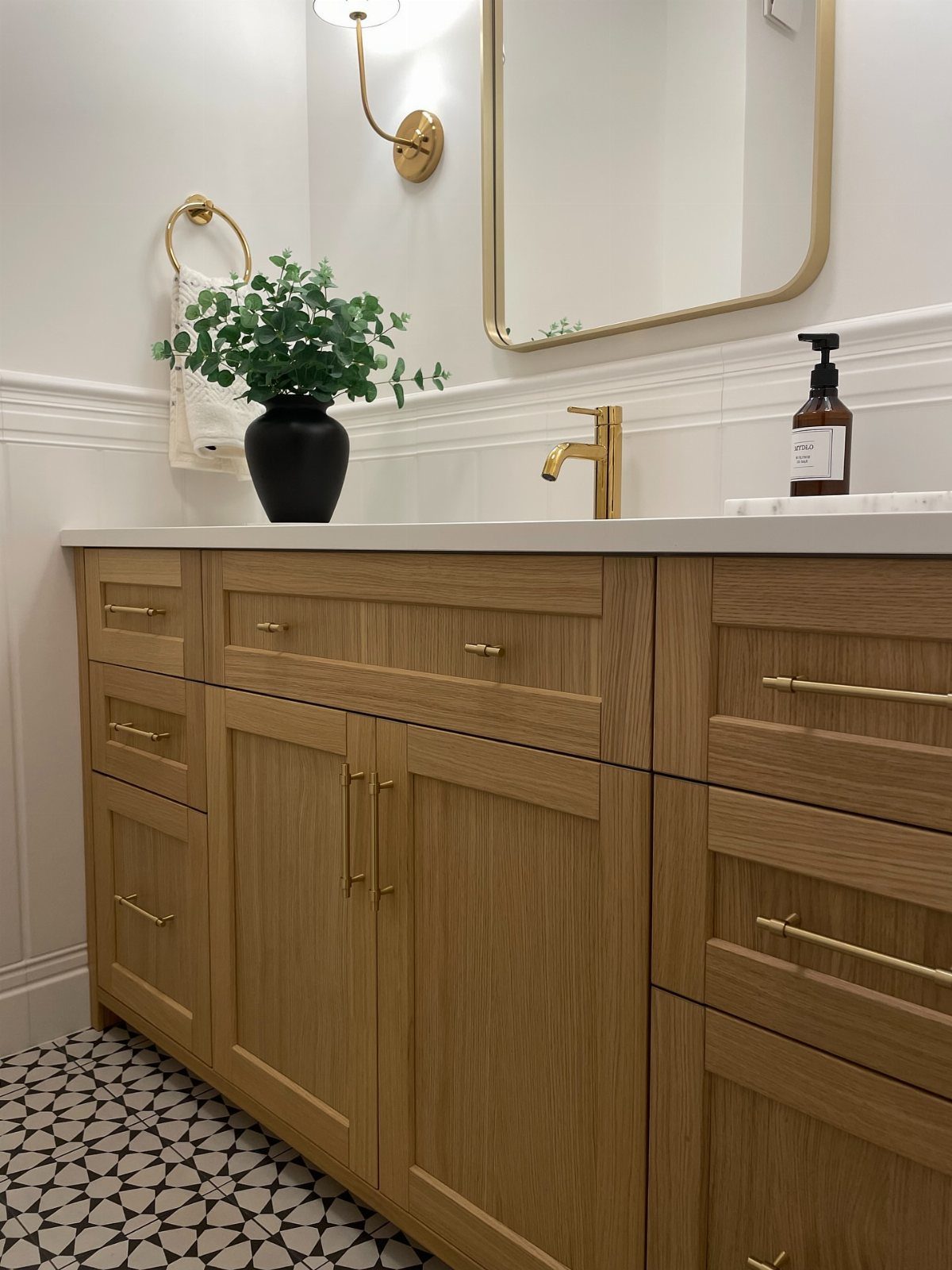 Light wood grain bathroom vanity with gold hardware and a white countertop in a bright room.