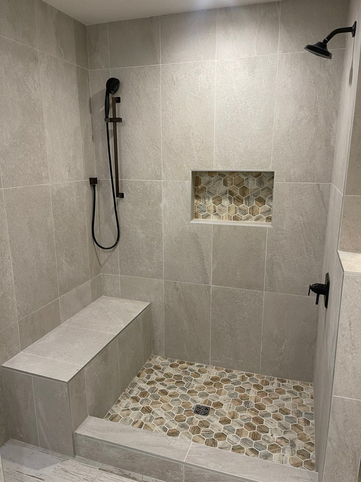 A walk-in shower featuring grey wall tiles, a pebble mosaic floor, and a built-in stone bench.