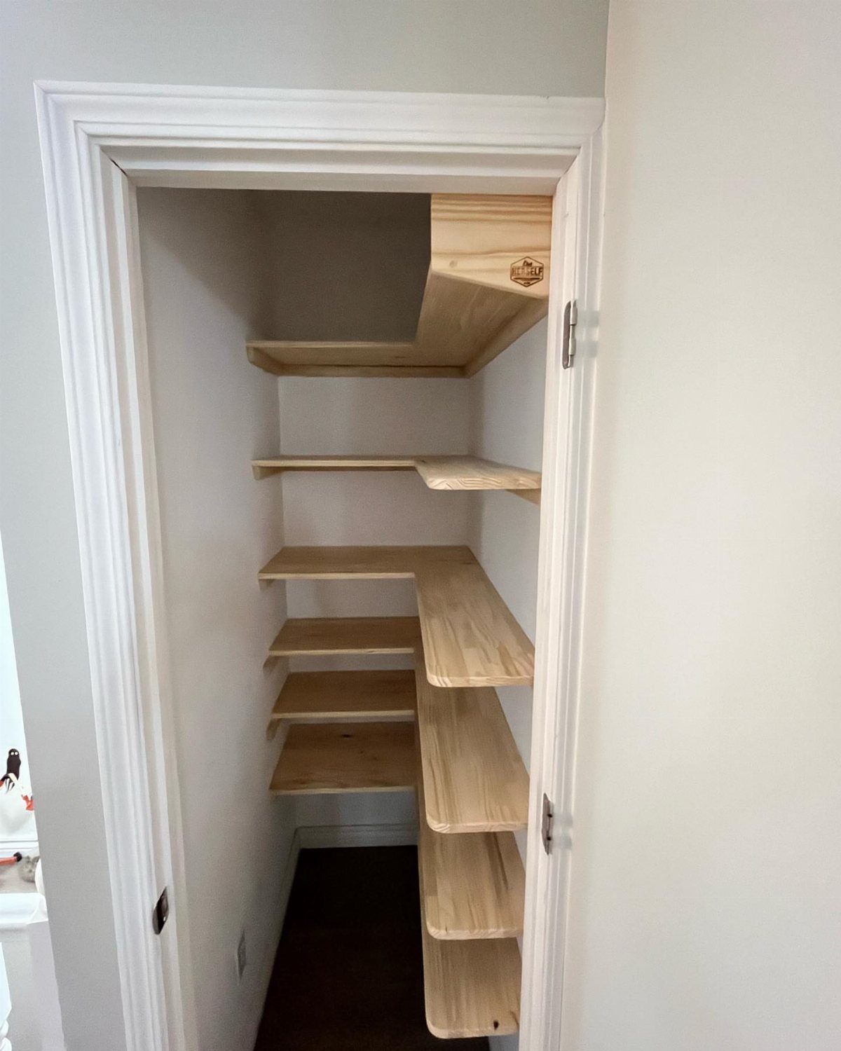 Wooden L-shaped shelves installed inside a narrow white closet for storage.