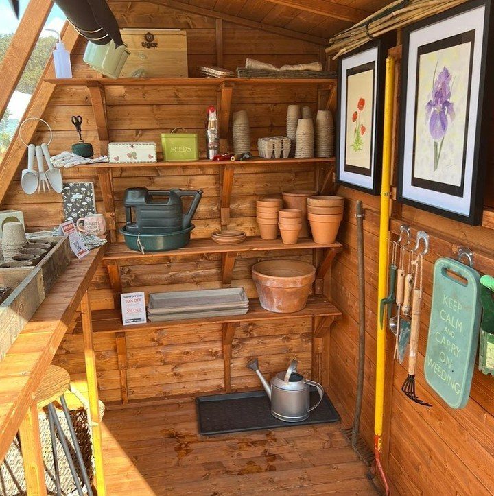 Wooden shelves inside a garden shed filled with terracotta pots and various gardening supplies.