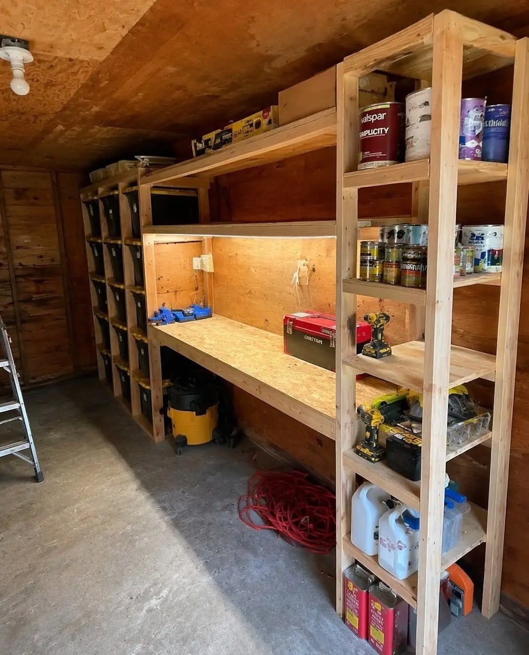 Wooden shelving units and a workbench filled with tools and paint cans inside a shed.