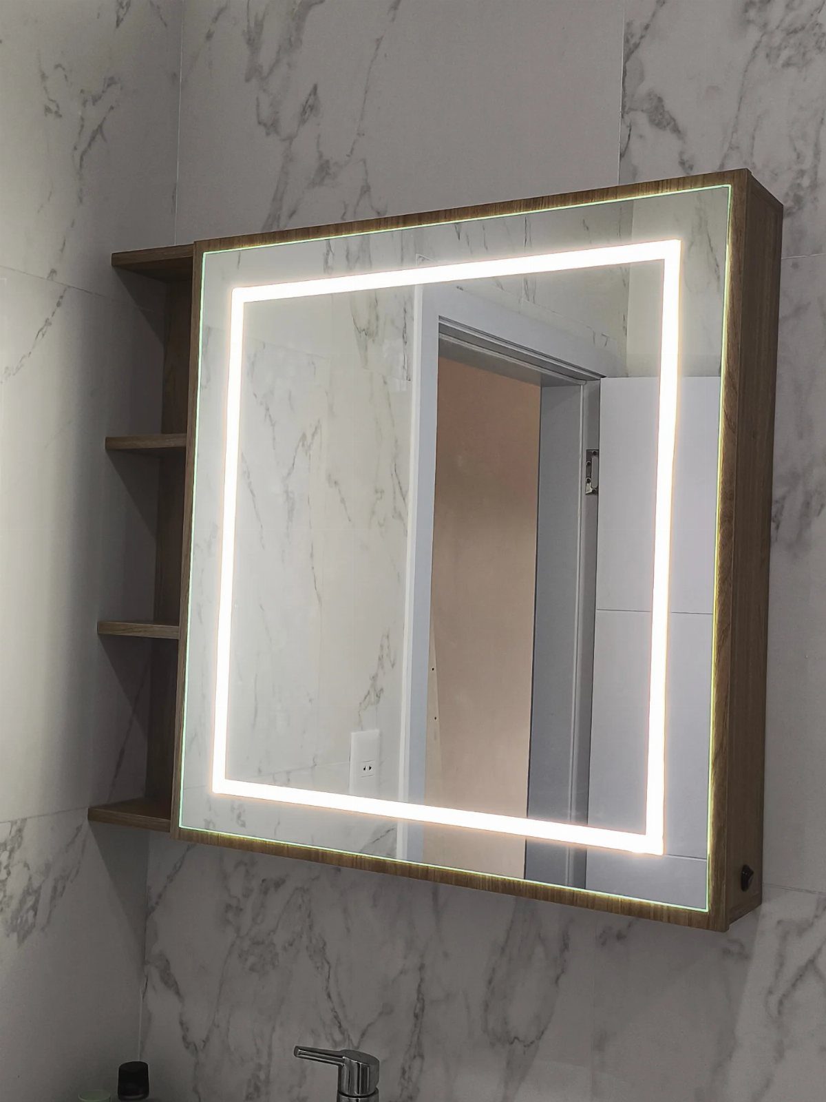 A wooden wall-mounted medicine cabinet with an integrated rectangular LED light strip on marble tiles.