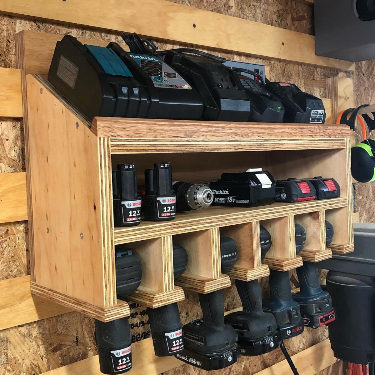 Wooden wall-mounted shelf organizer holding multiple black power tool batteries in various compartments.
