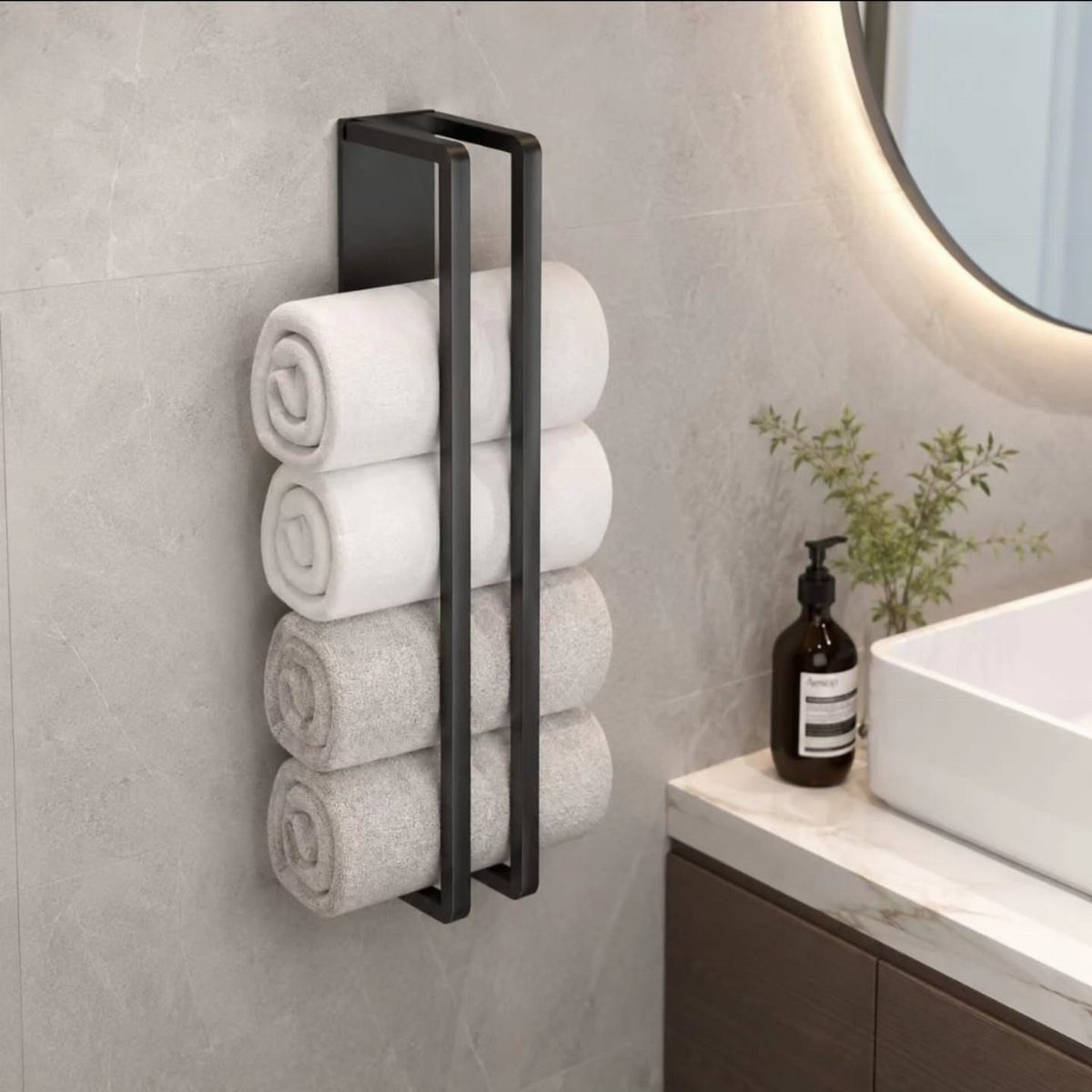 Black wall-mounted metal towel rack holding four rolled white and grey towels on a grey wall.